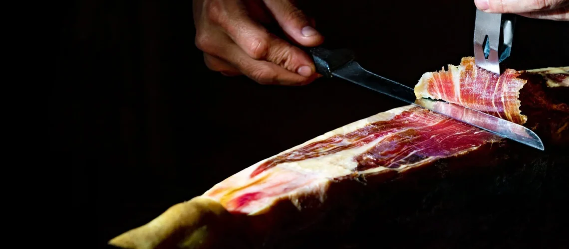 gastronomia-comida-espana-detalle-primer-plano-maestro-cortador-jamon-iberico-sobre-fondo-oscuro-sca.webp